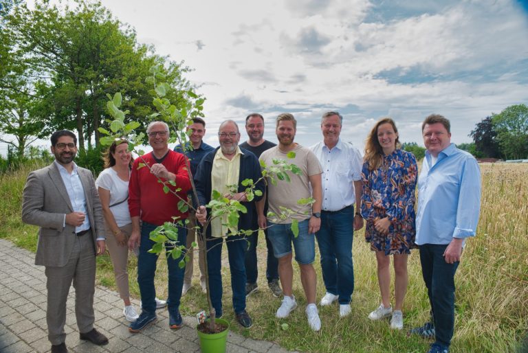 Gruppe von Menschen mit Pflanzen, auf einer Wiese unter einem bewölkten Himmel.