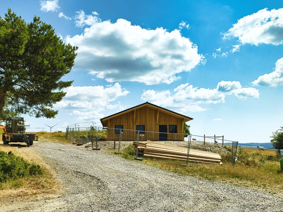 Hölzerne Hütte auf einem Feldweg unter blauem Himmel und Sonne.