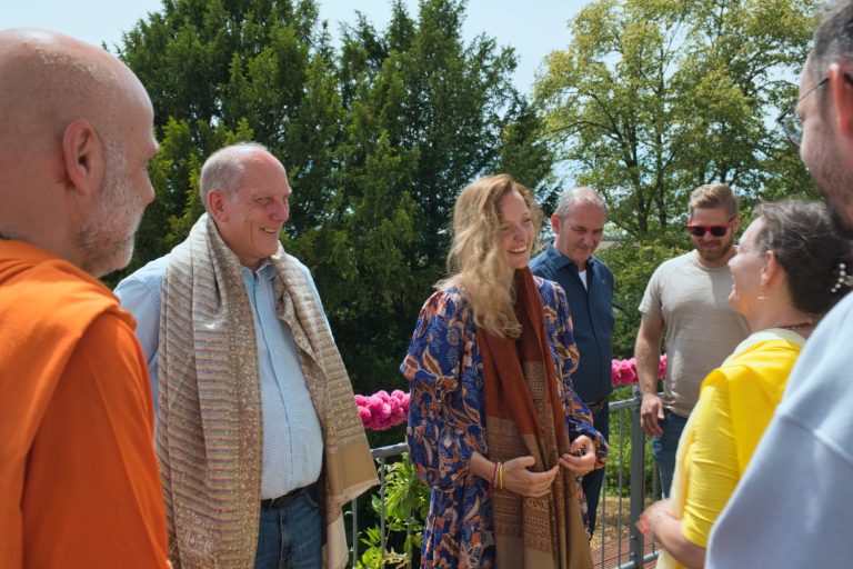 Gruppengespräch im Freien, Teilnehmer in lässiger Kleidung, umgeben von Pflanzen.