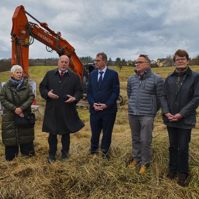 Gruppenszene mit fünf Personen und einem Bagger in ländlicher Umgebung.