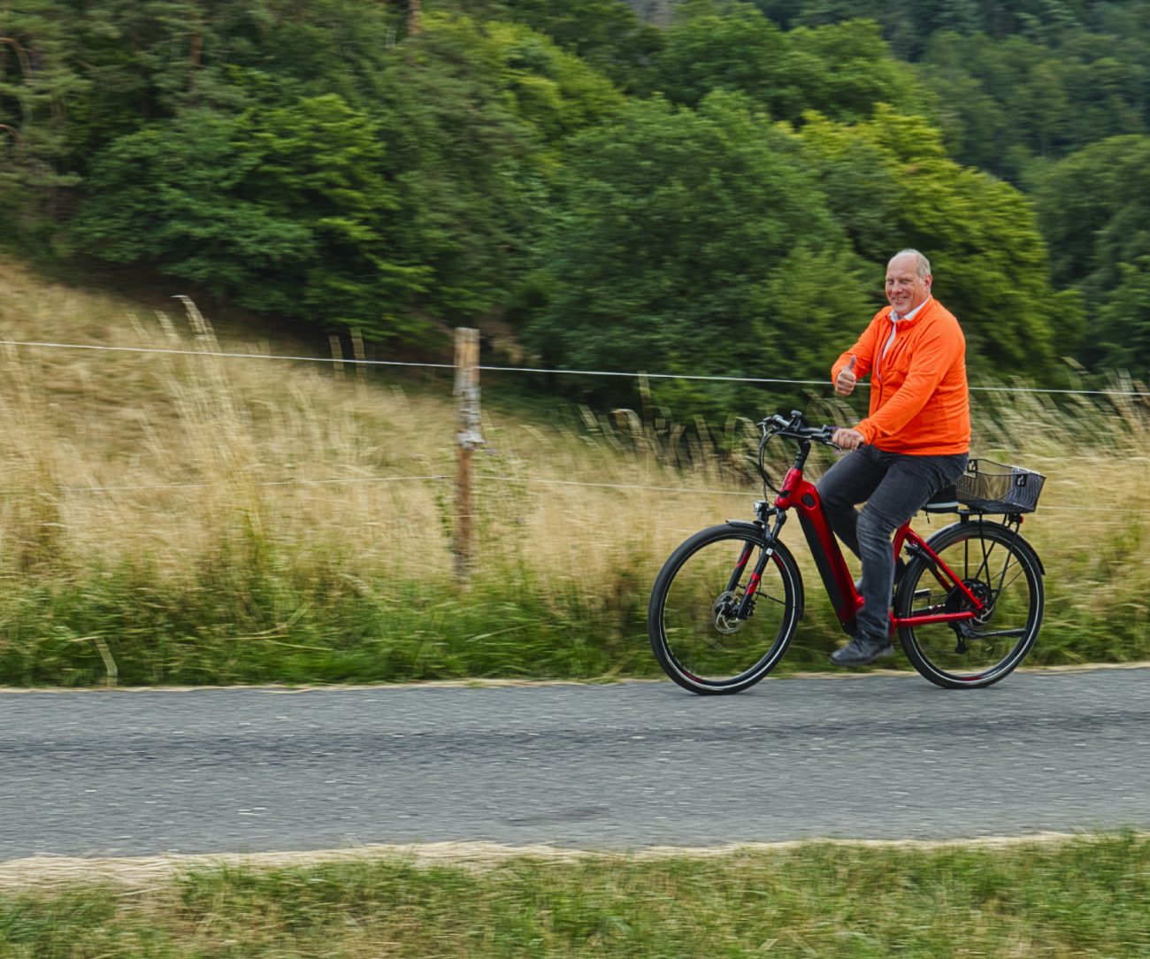 Mann in orangeem Pullover fährt auf einem roten E-Bike entlang einer Straße.