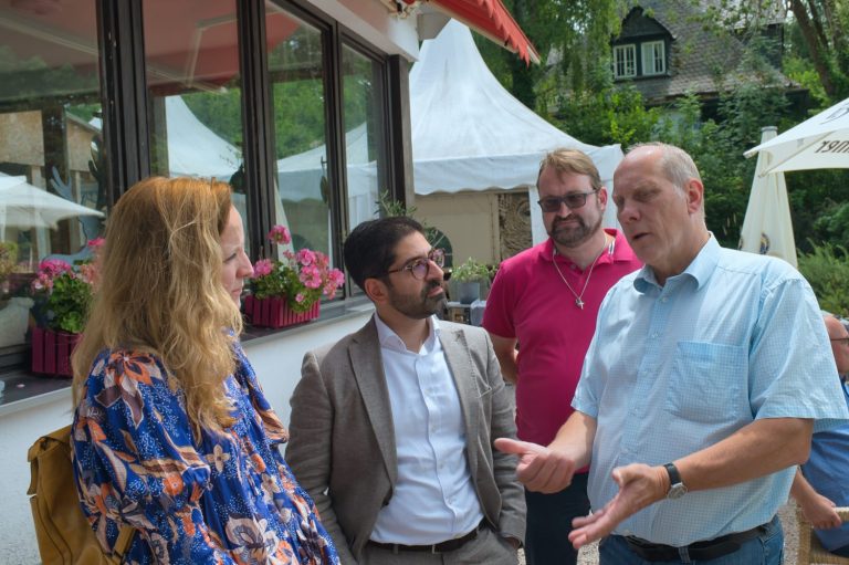 Vier Personen stehen im Freien und unterhalten sich, umgeben von Blumendekorationen.